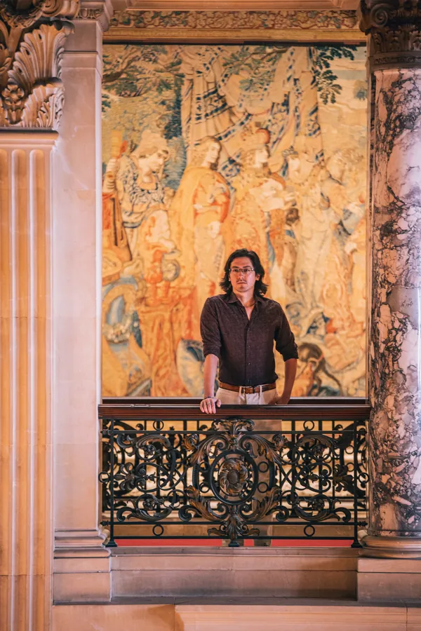 Man in a burgundy shirt before a gilded tapestry